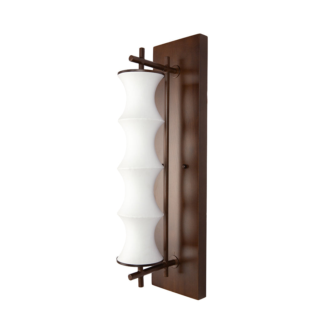 Vintage light wall fixture installed in a dimly lit hallway, with the soft illumination highlighting the subtle grain of the wood panel.