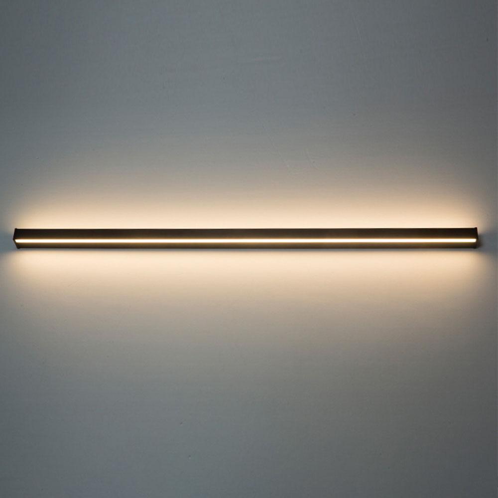 Horizontal linear outdoor wall sconce with warm illumination, mounted above a modern bed for ambient lighting.