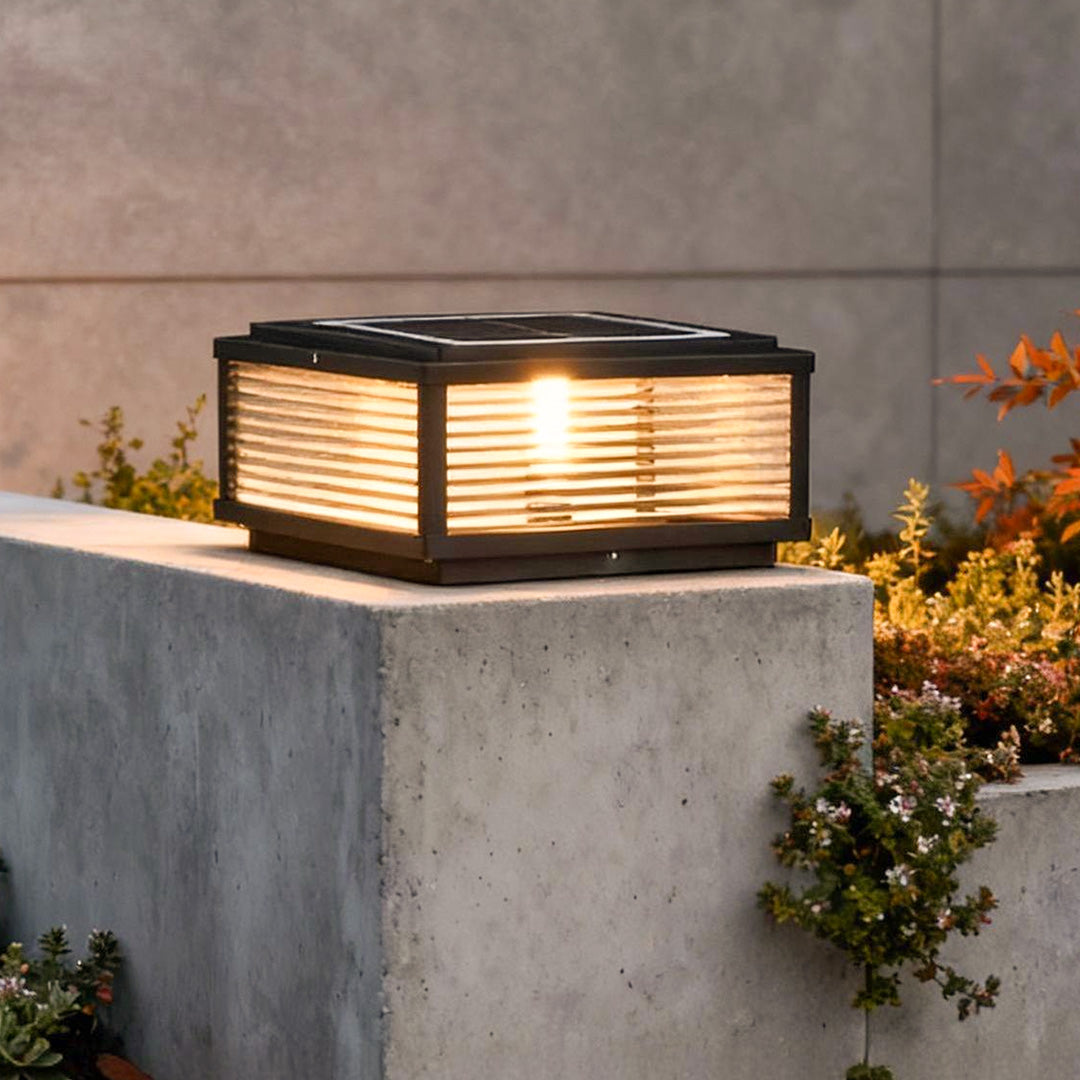 Square pillar light with horizontal slats, mounted on concrete pillar for warm and modern outdoor pathway illumination.