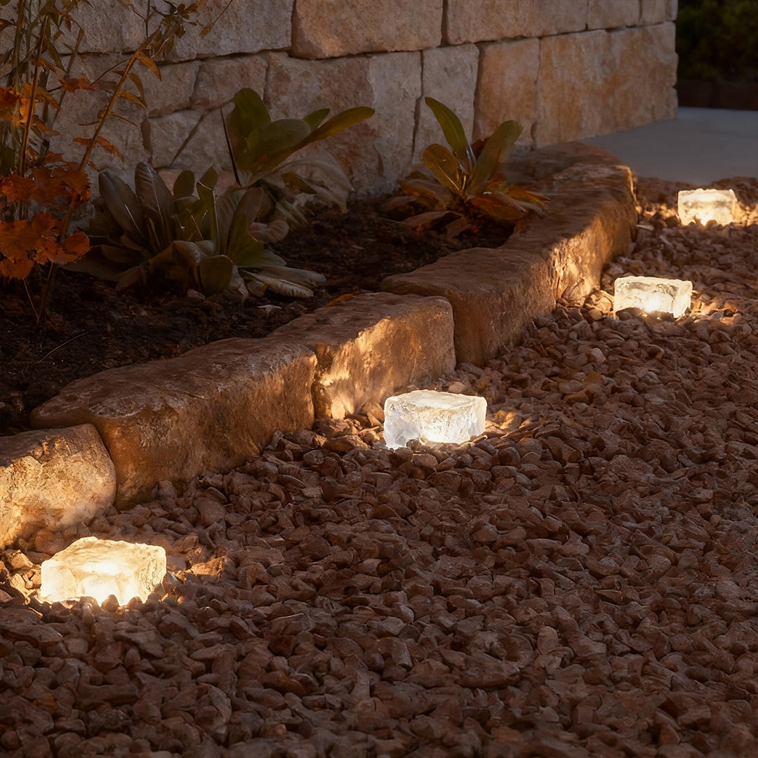 Ice cube landscape lights placed along a stone garden border with warm glow.