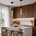 Industrial style pendant light fixtures hanging above a modern kitchen island, featuring black metal frames and warm Edison bulbs.
