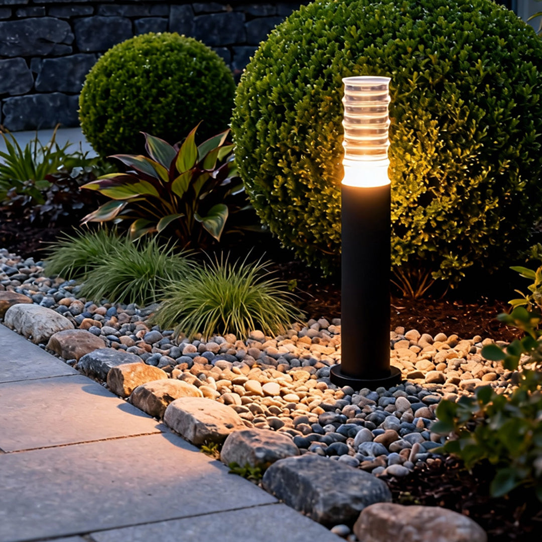Black landscape lighting bollard lighting up a landscaped garden with decorative stones and trimmed shrubs.