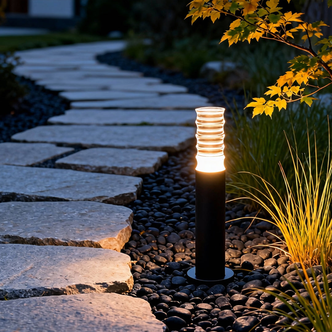 Landscape lighting bollard illuminating a curved stone pathway with warm light, creating an inviting garden atmosphere.