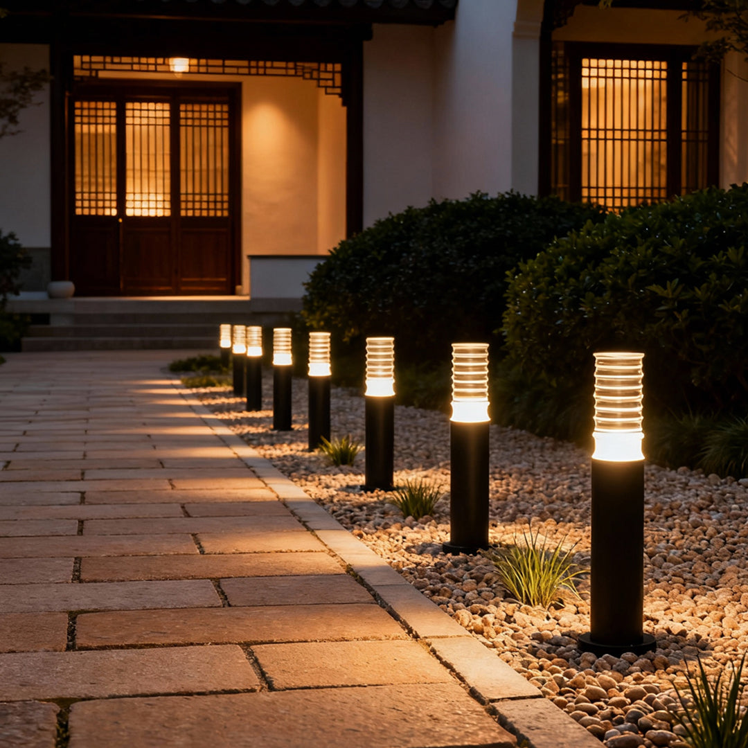 Series of warm-lit landscape lighting bollards guiding the walkway to a modern house entrance in the evening.