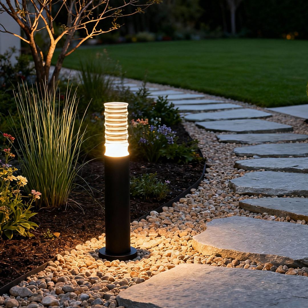 Warm-glow landscape lighting bollard installed near lawn edges along a nighttime garden path.