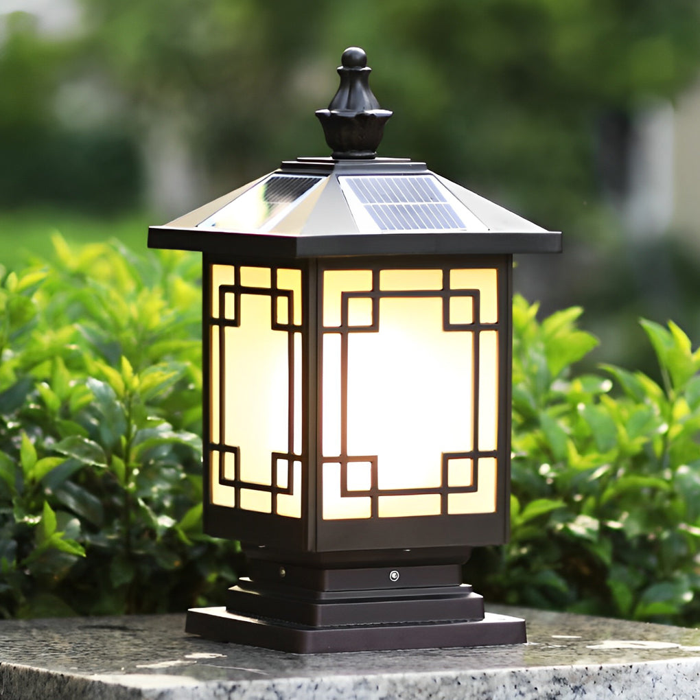 Lantern pillar lights placed on a stone pillar surrounded by lush green shrubs.