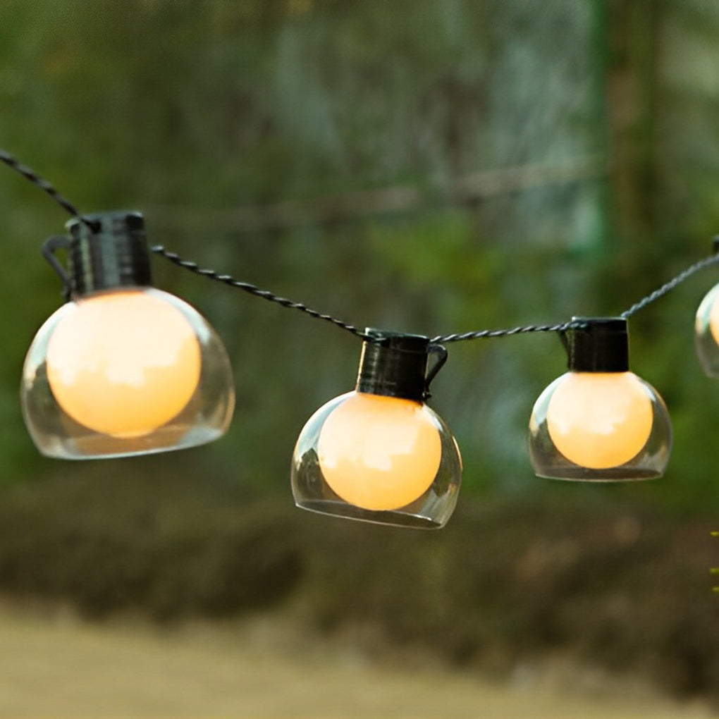 LED globe string lights displayed among palm leaves, blending warm lighting with lush garden greenery.