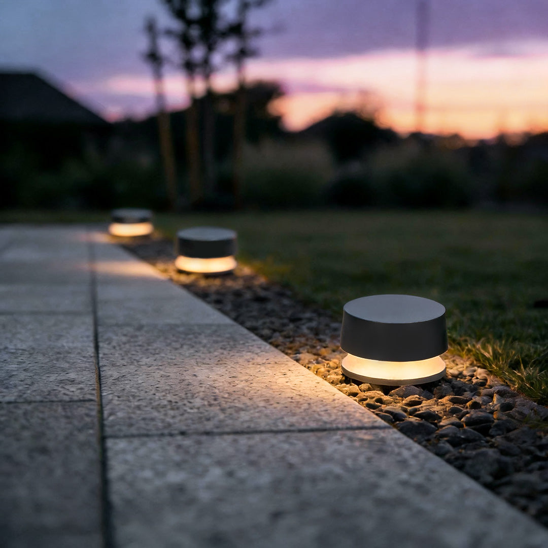 Low-profile LED outdoor landscape lights lining a paved walkway at dusk, providing subtle guidance and ambient illumination.