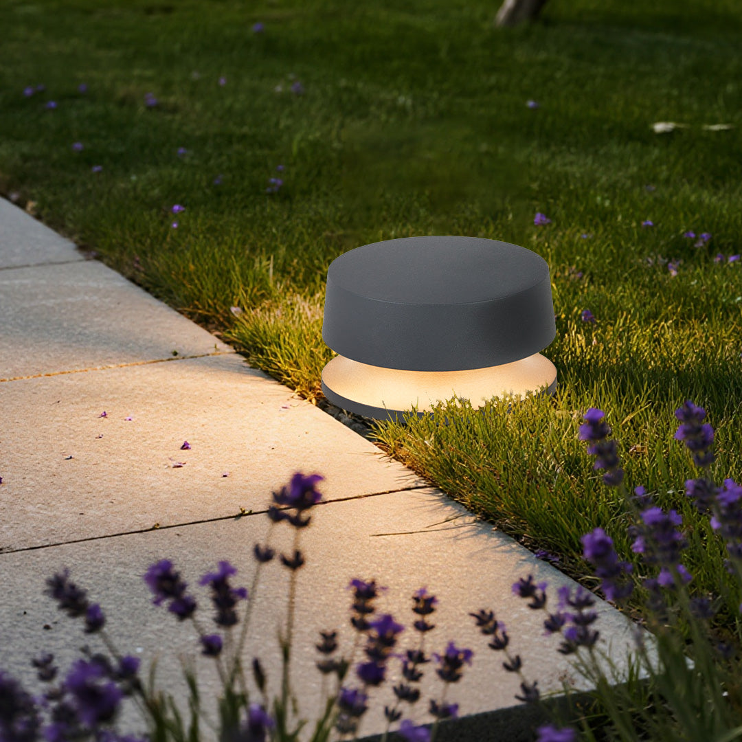 Round LED outdoor landscape lights placed along a concrete garden path, blending into lawn edges with warm diffused lighting.