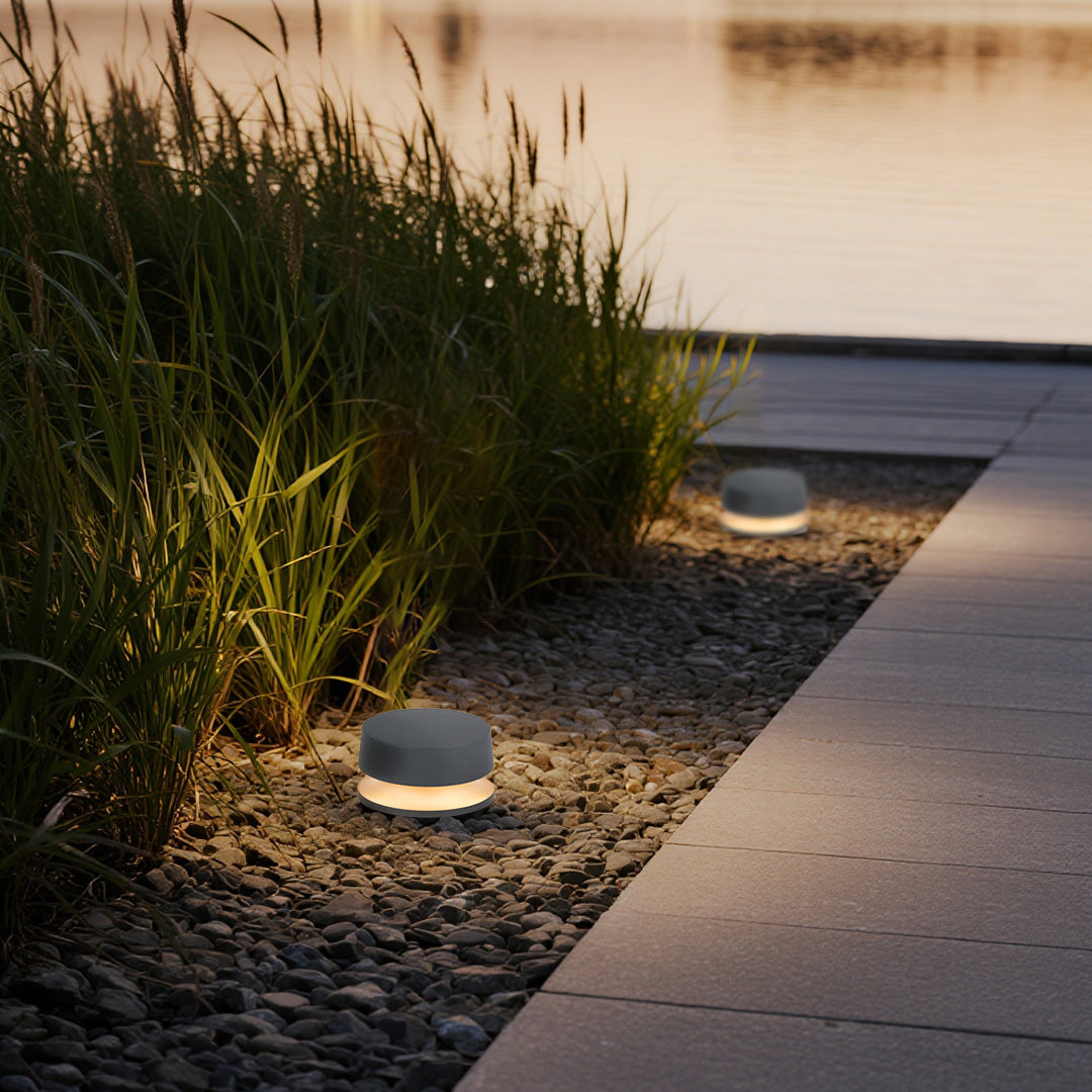LED outdoor landscape lights installed beside a waterside path, casting a soft warm glow on grass and stone edges in a modern garden.