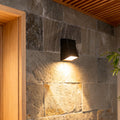 LED outdoor wall sconce mounted on a stone wall, providing warm and focused illumination.