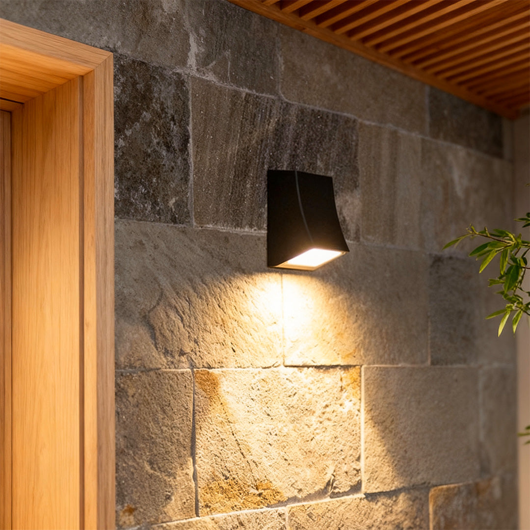 LED outdoor wall sconce mounted on a stone wall, providing warm and focused illumination.