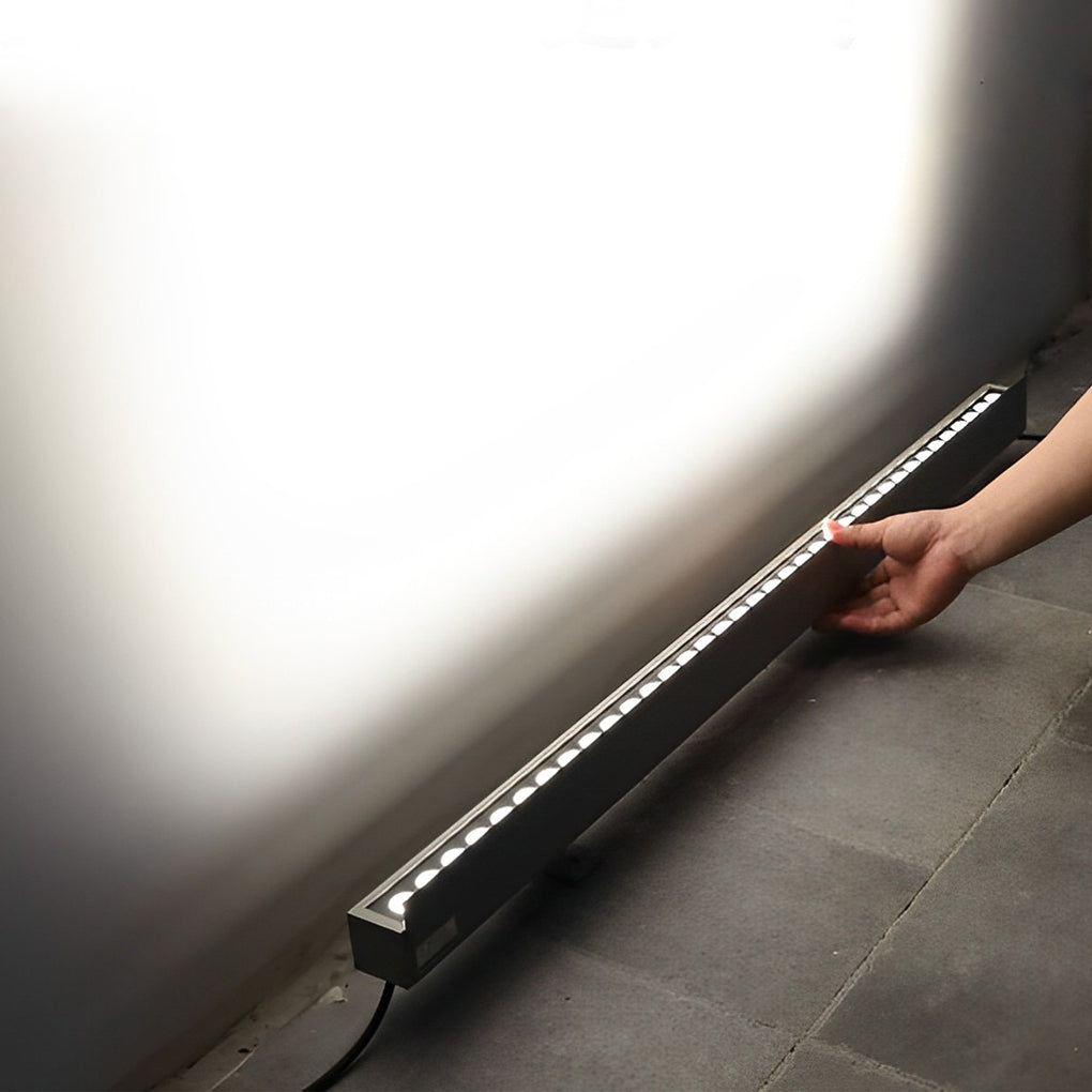 Linear LED wall washer emitting bright white light along a concrete wall for accent lighting.
