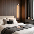 Modern long linear wall sconce installed beside bed with warm vertical LED ambient lighting.