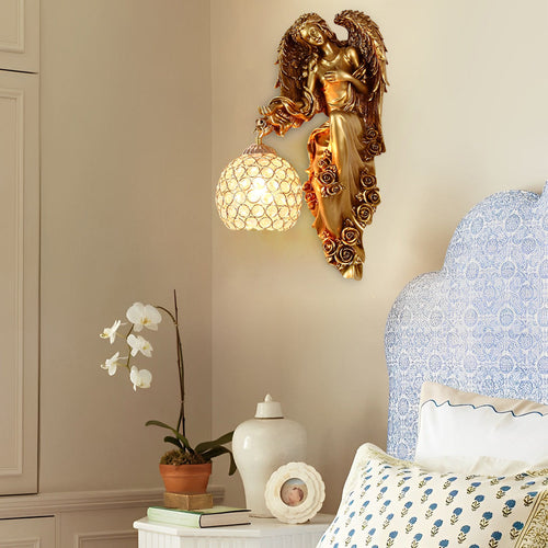 Luxury angel wall sconce installed beside bed featuring gold angel sculpture and crystal globe lamp.