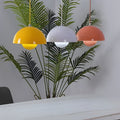 Metal dome pendant light in pastel colors, hanging above indoor plant on modern shelf.