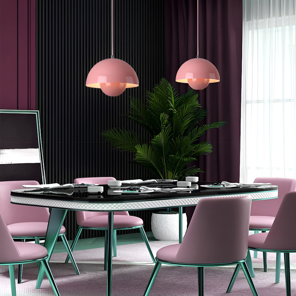 Metal dome pendant light in pink, hanging above contemporary dining table with green chairs.