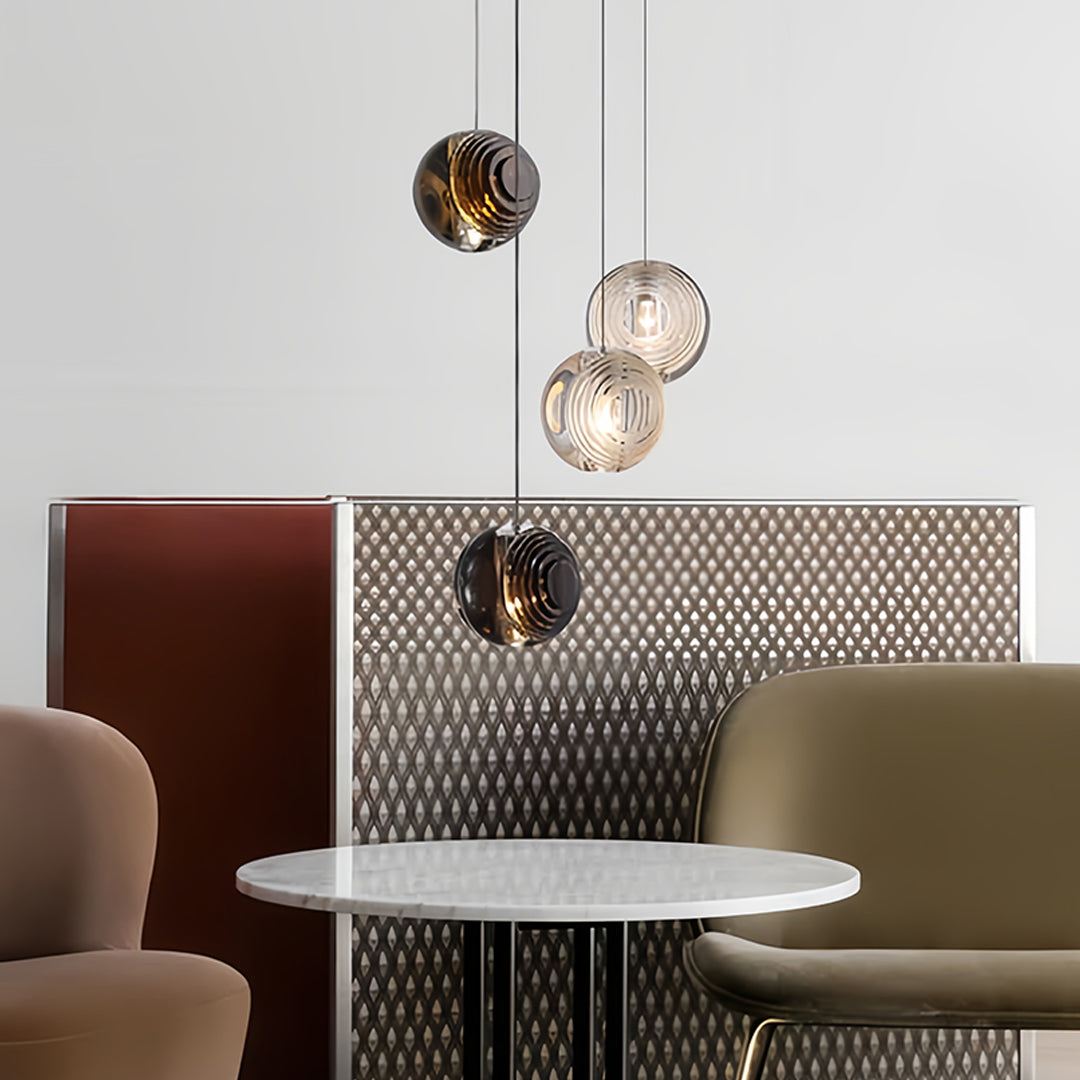 Metal pendant lights with smoked glass shades hanging above a round table in a contemporary lounge area.