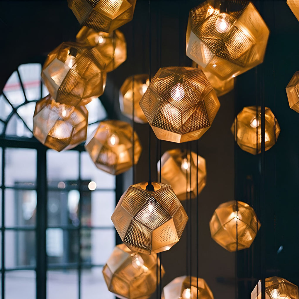 Close-up view of a metal shade pendant light with perforated geometric panels glowing warmly in a dark interior.