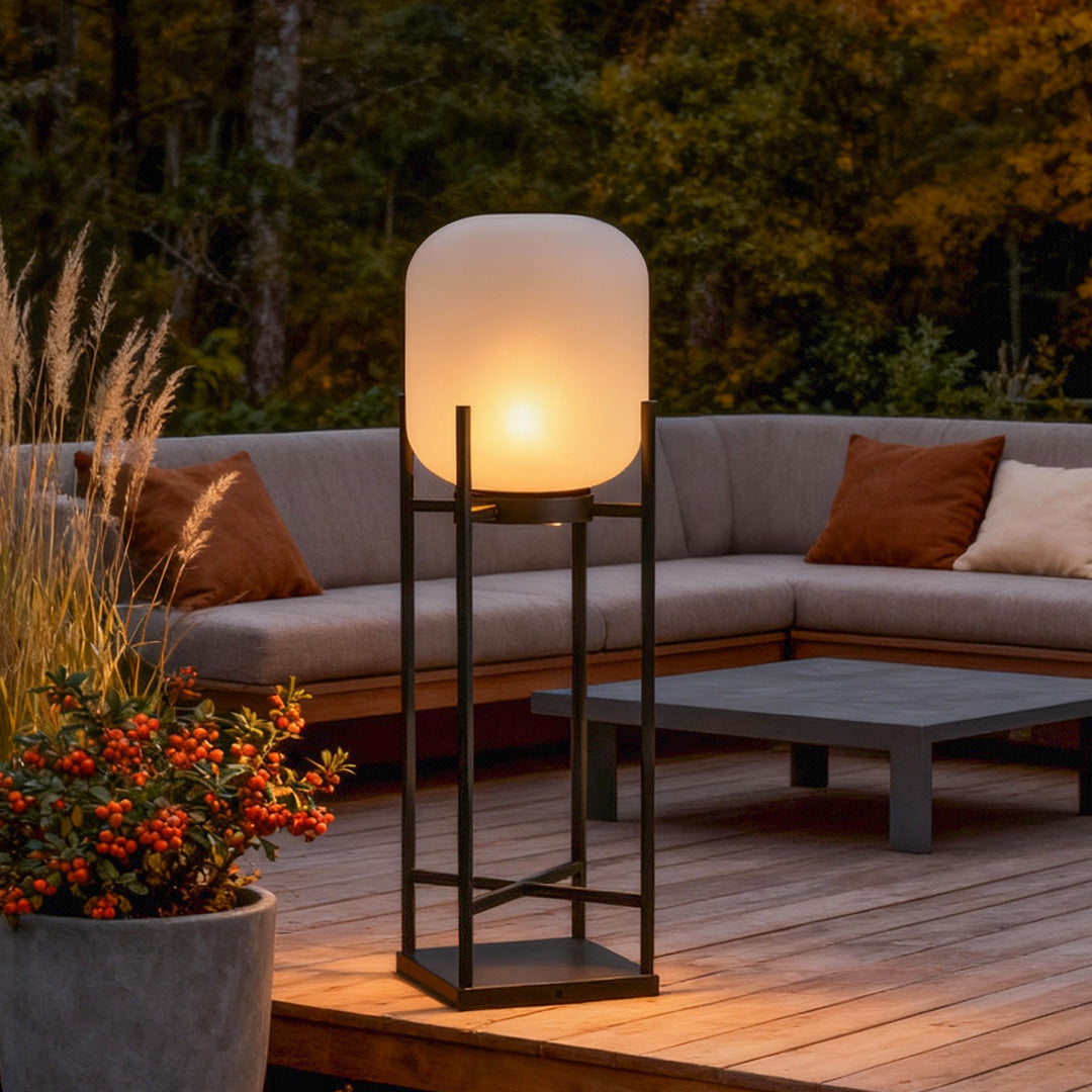 Outdoor standing light with minimalist black frame and frosted shade in garden with ornamental grass.