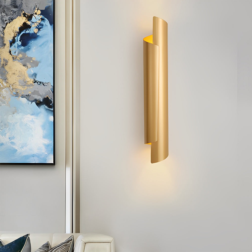 Minimalist scroll wall sconce in gold, casting warm light on a white wall in a contemporary setting.