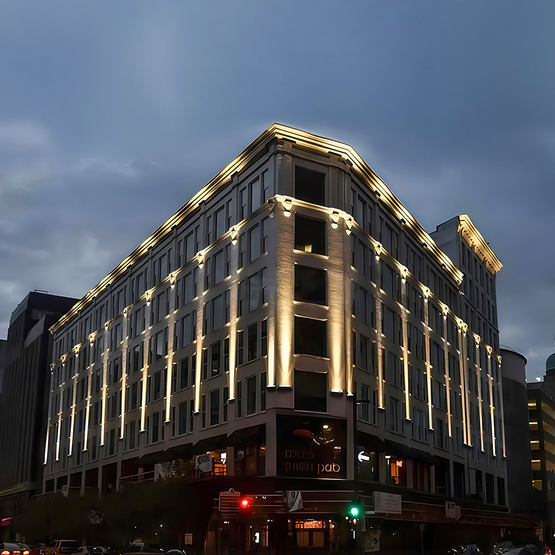 Modern commercial building facade using vertical architectural flood lights for dramatic uplighting at dusk.