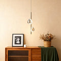 Modern crystal pendant light mounted above wooden credenza with decorative dried flowers in neutral interior