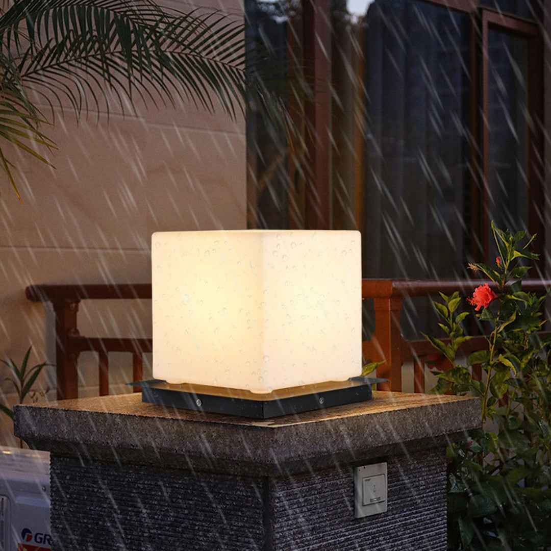 Silver Metal Table Lamp modern cube pillar light with warm white LED glow positioned on contemporary outdoor stone surface