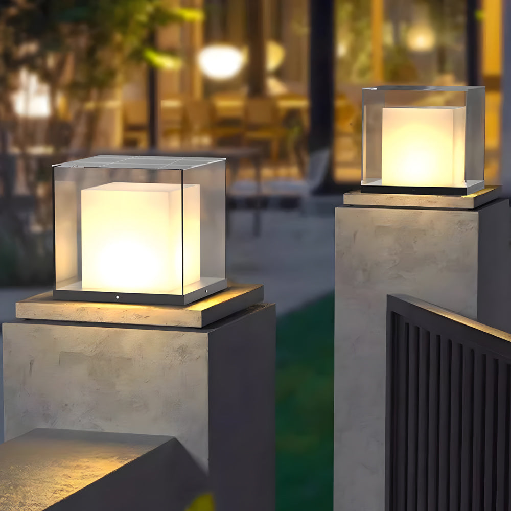Modern gate pillar light with a sleek cube design, illuminating a garden pathway at dusk.