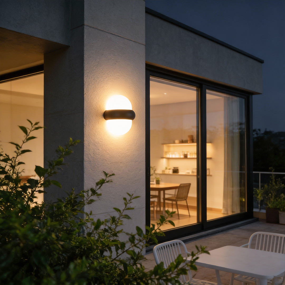 Modern globe wall sconce with sleek black frame, providing warm illumination near a contemporary patio.