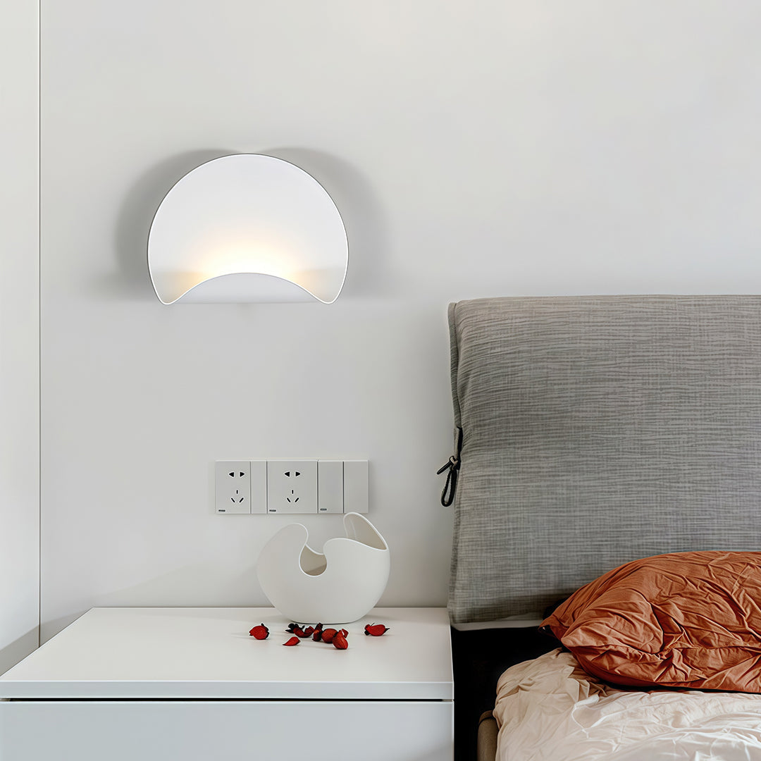 Modern half-moon white wall lights installed above a bedside table in a contemporary bedroom with neutral tones and minimalist decor.