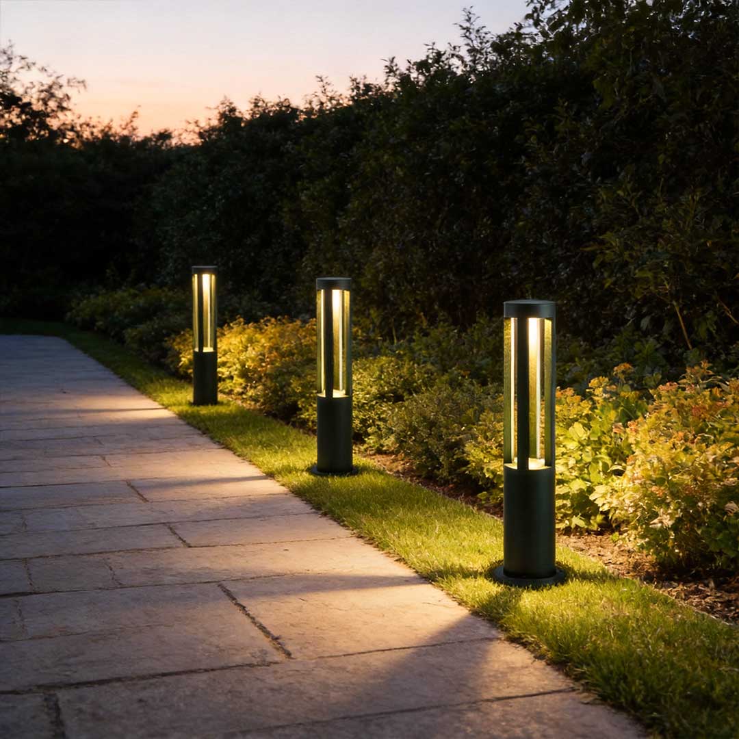 Modern outdoor bollard lights providing soft light along a paved walkway at dusk.