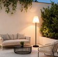 Modern outdoor floor lamps illuminating a cozy patio seating area with wicker furniture and greenery.