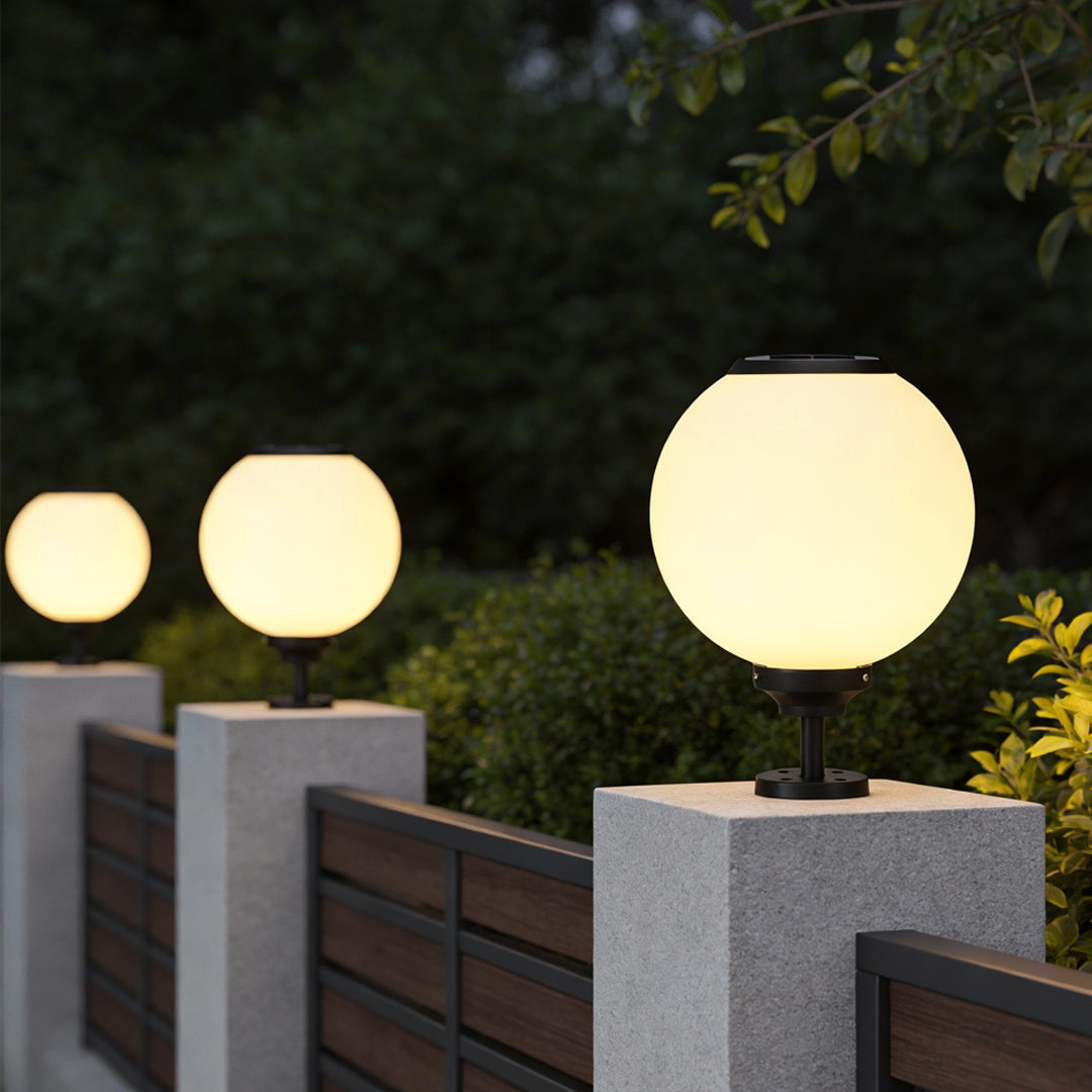 Modern outdoor gate pillar light with a spherical design, providing warm illumination on a wooden fence.