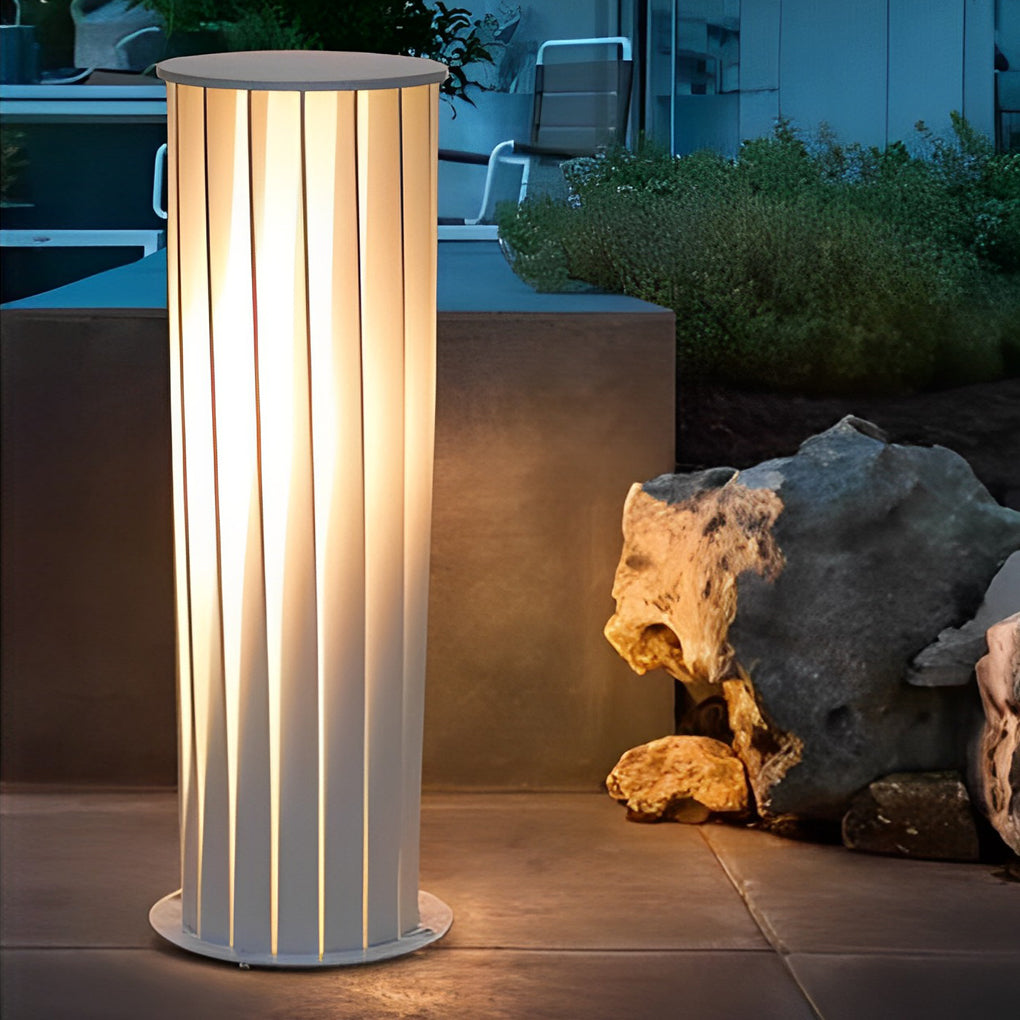 Tall cylindrical modern outdoor lanterns with soft ambient glow placed beside poolside stone feature.