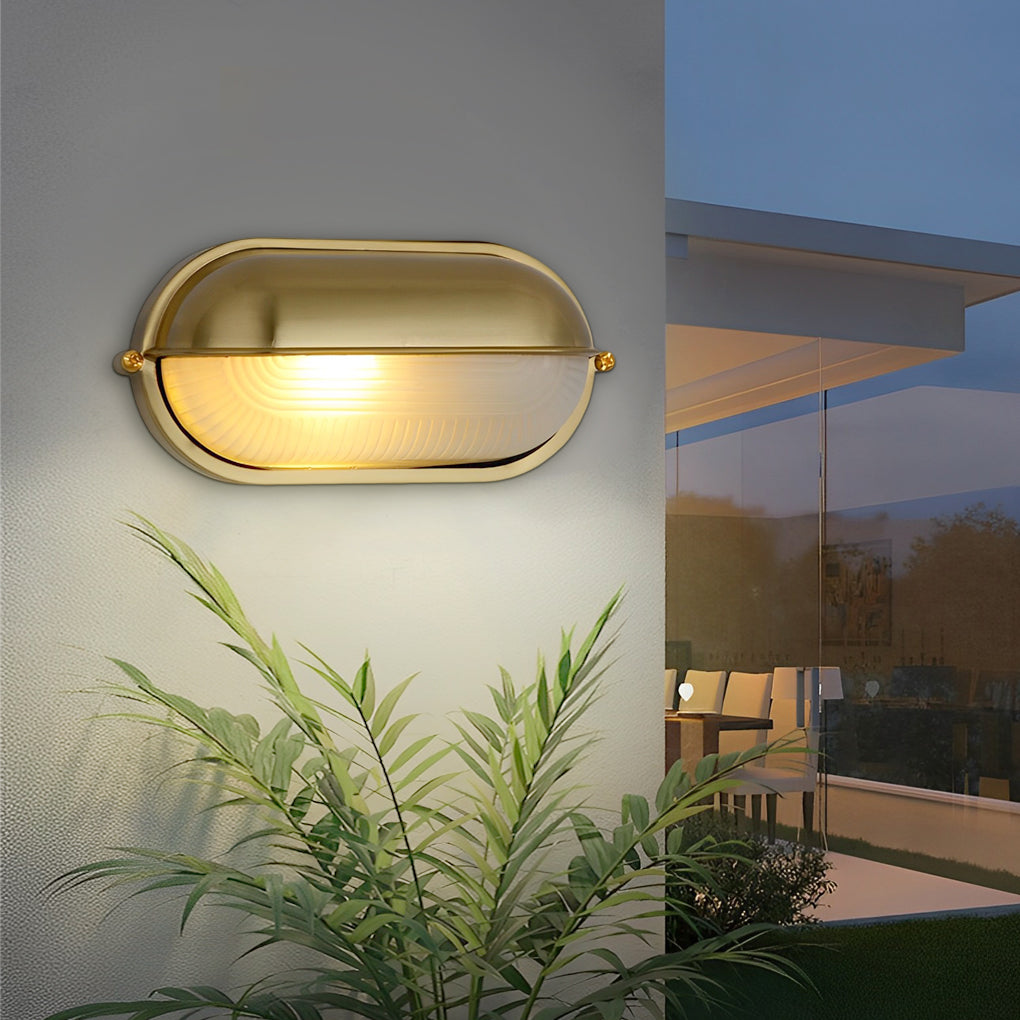 Modern oval bulkhead light mounted on an exterior wall near plants, emitting soft warm lighting.