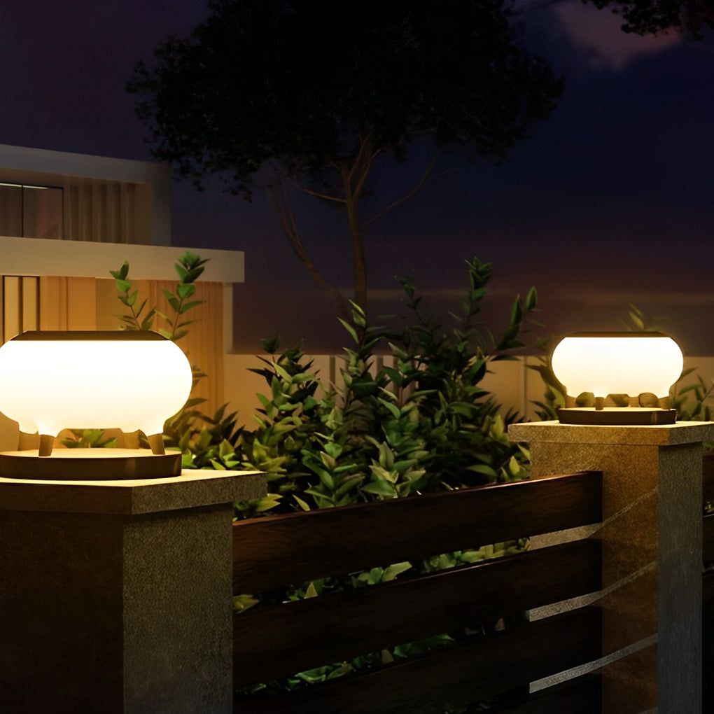 Modern solar column pillar lights installed on concrete pillars, illuminating a garden fence and plants.