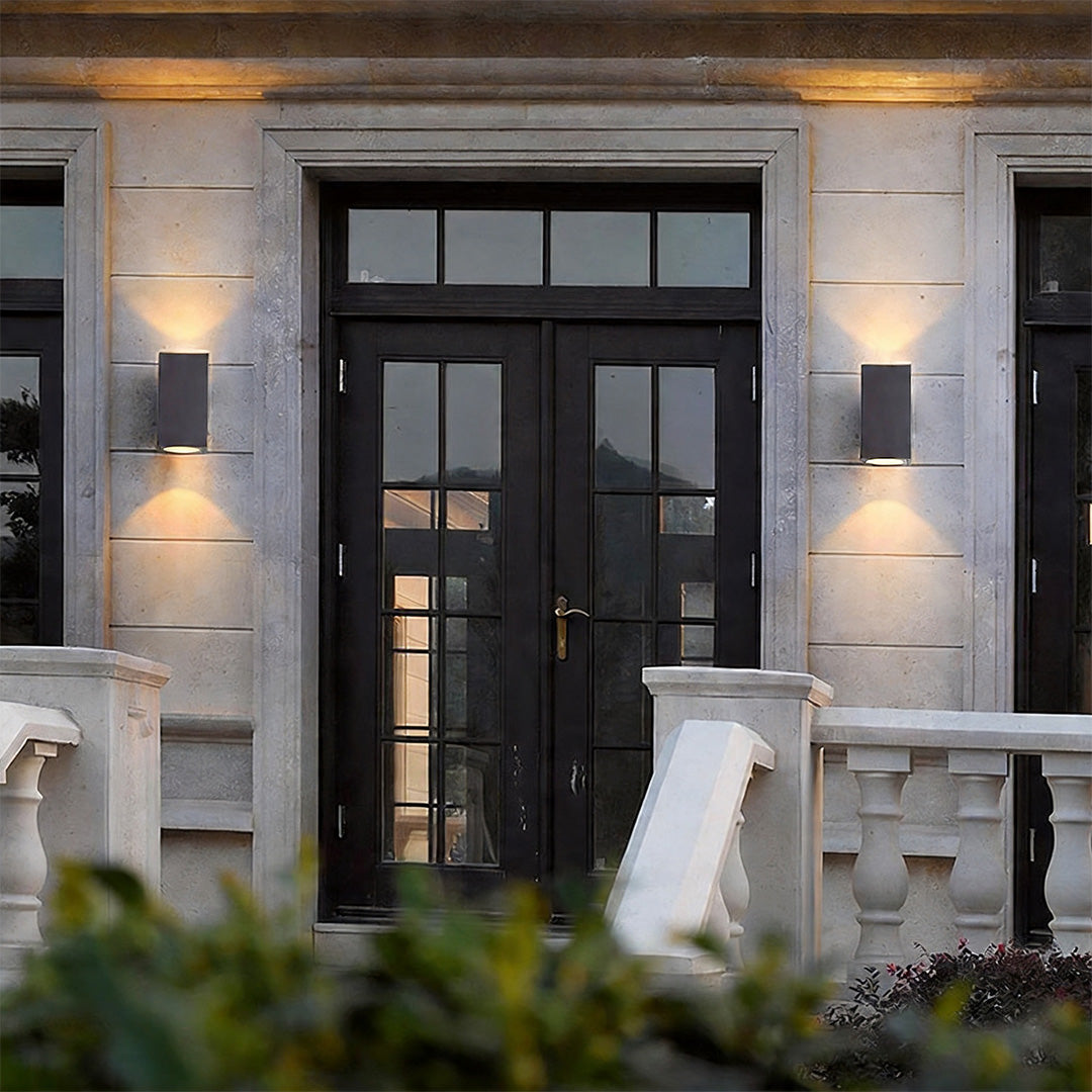 Modern wall sconce up and down light fixtures flanking a dark double door on a stone facade.