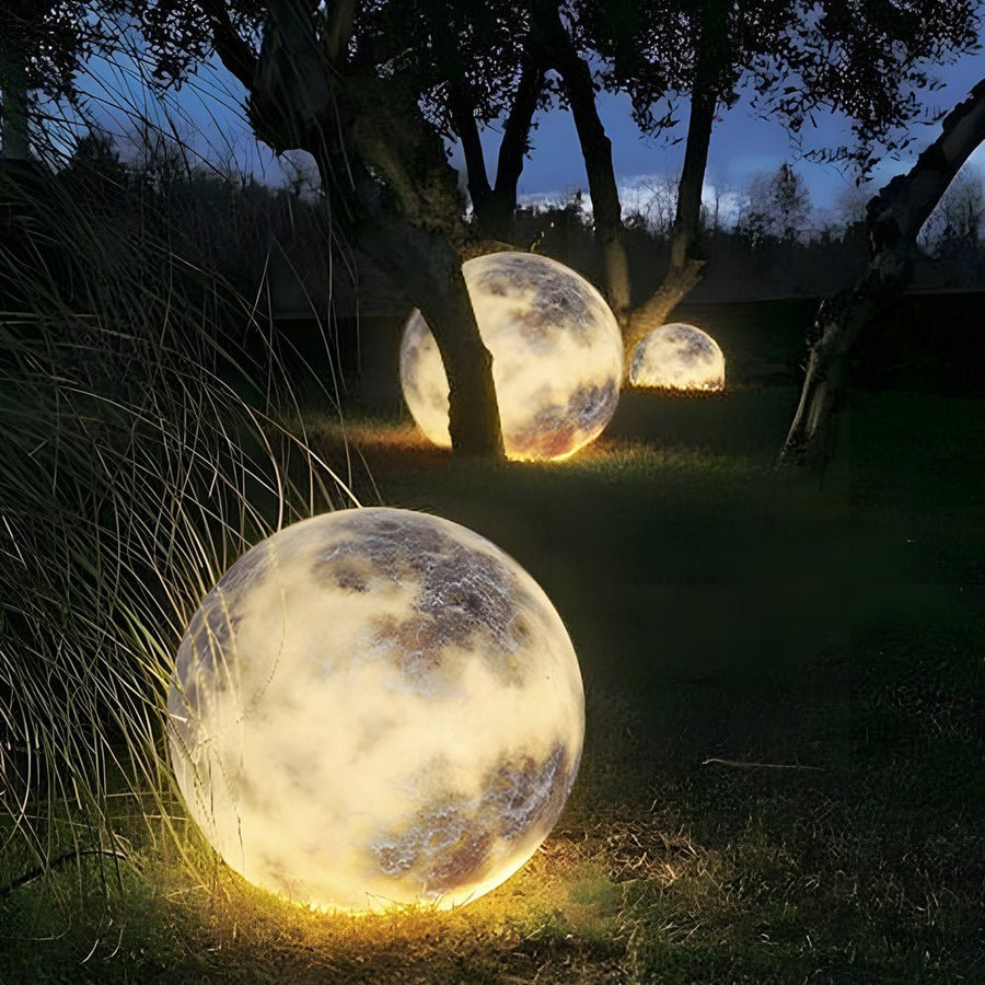 Moon light sphere placed under trees in a nighttime garden.