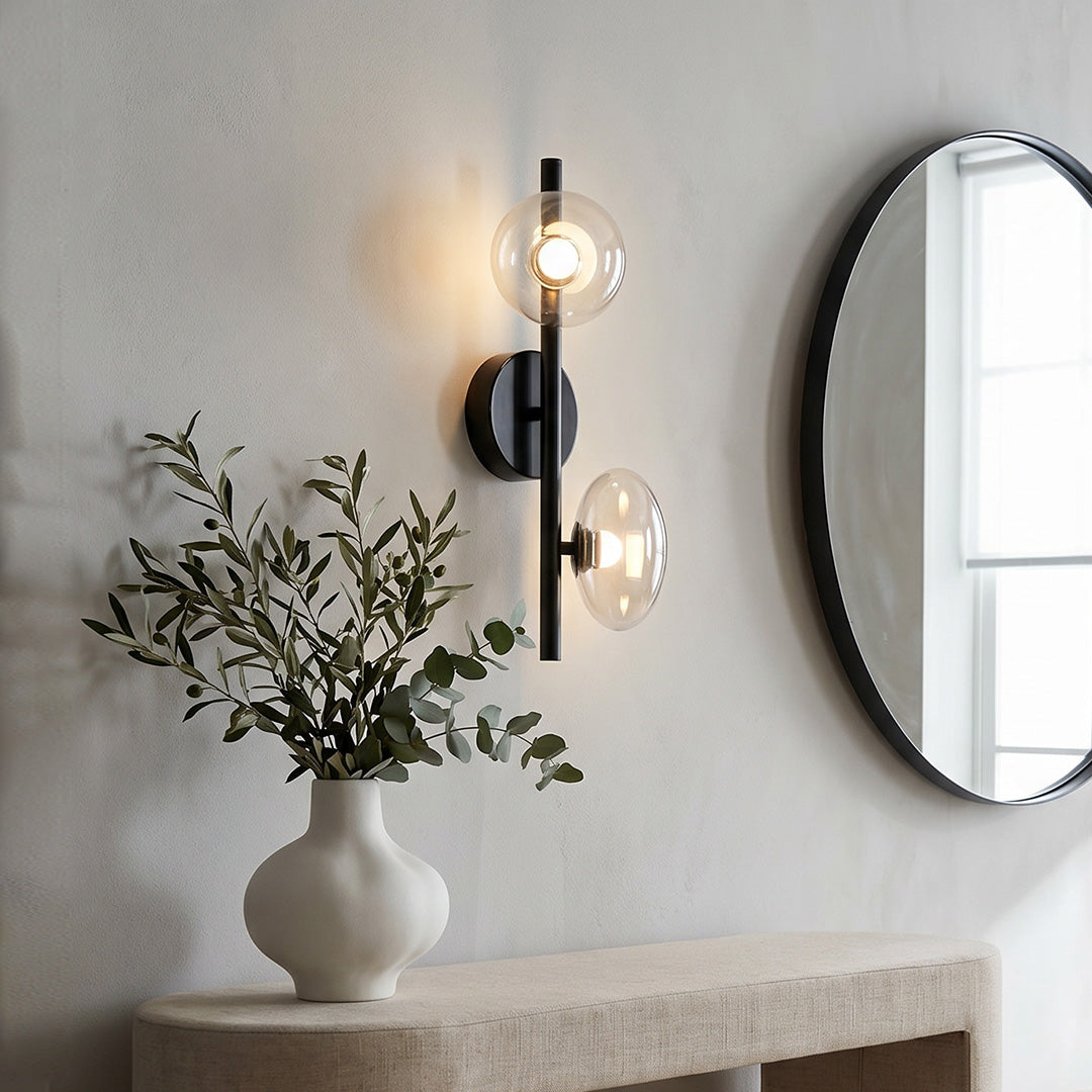 Multi light wall sconce mounted beside a mirror in a modern bathroom with soft ambient lighting.