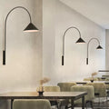 Multiple wall arm lights with varying curved stems and cone shades illuminating modern cafe dining area.