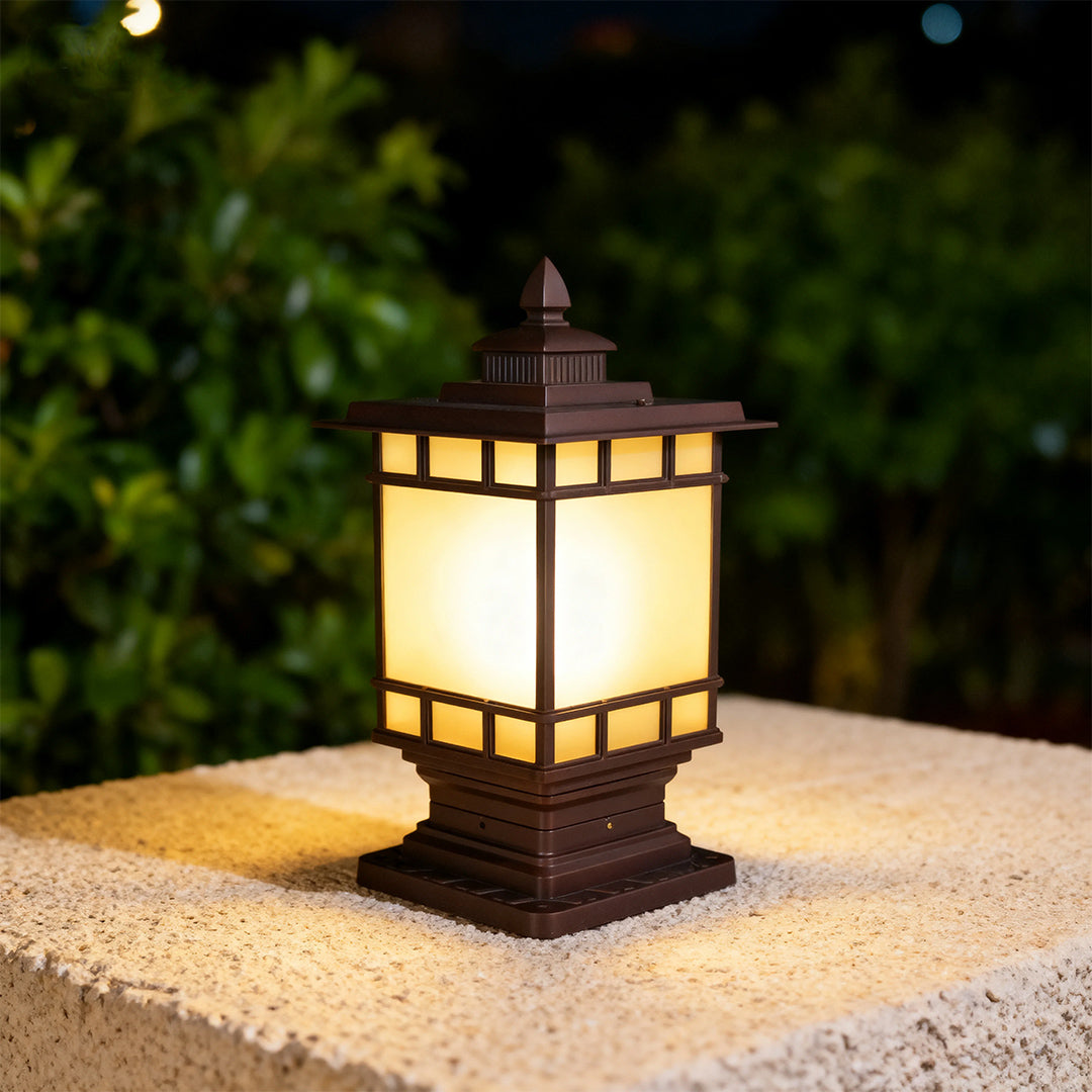 Oriental style metal pillar light glowing warmly on beige column against dark evening garden backdrop