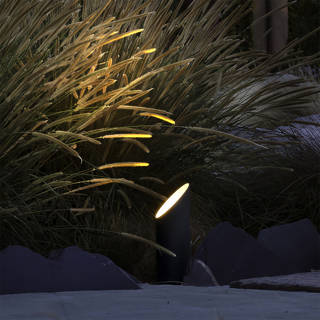 Landscape tree up lighting fixture illuminating tall ornamental grasses and rugged stones with a warm, focused beam.