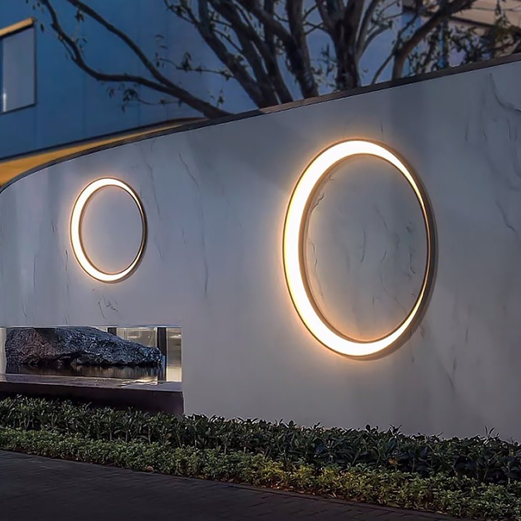 Outdoor cylinder wall light mounted on a garden wall, casting a warm circular glow along a landscaped exterior pathway.