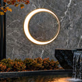 Outdoor cylinder wall light mounted on a stone wall beside a water feature, creating a soft circular glow for modern landscape lighting.