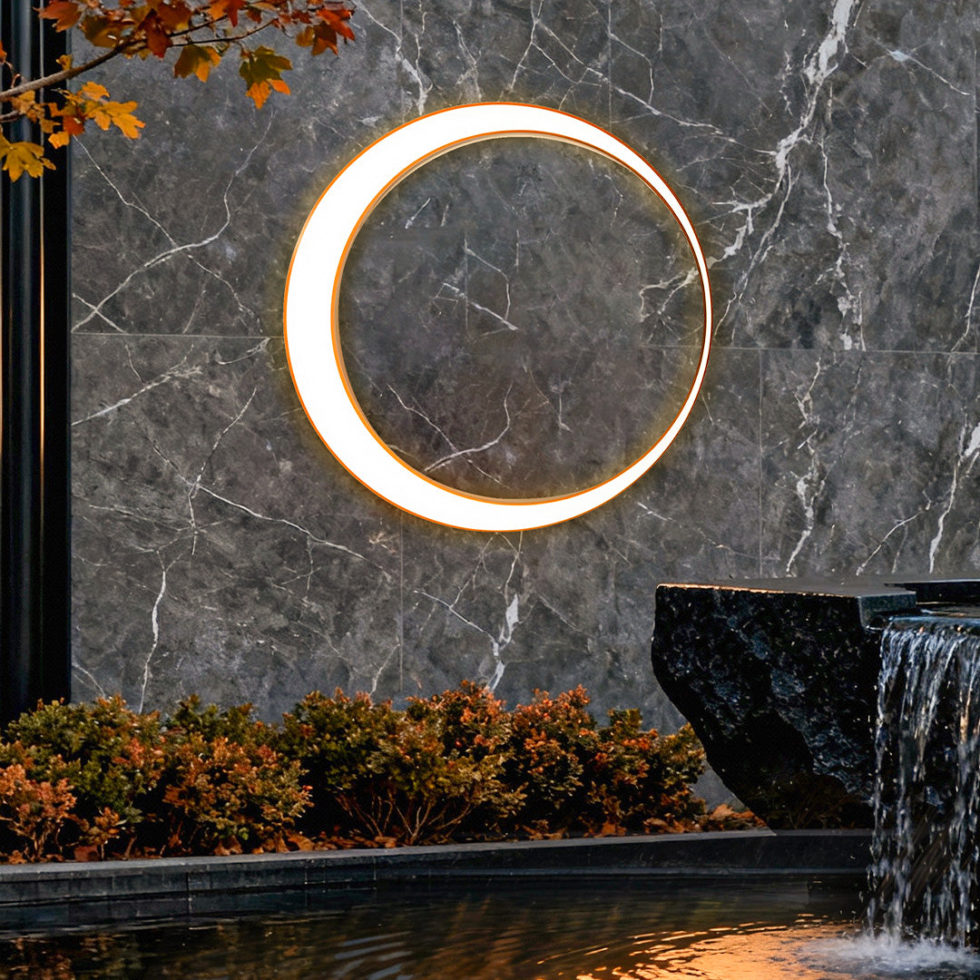 Outdoor cylinder wall light mounted on a stone wall beside a water feature, creating a soft circular glow for modern landscape lighting.