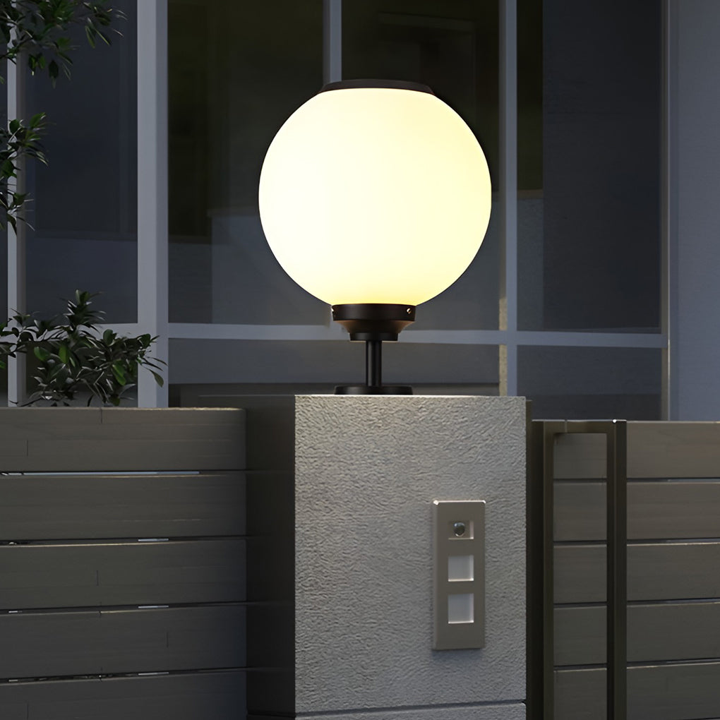 Outdoor gate pillar light with a spherical shape, casting a soft glow on a patio area for a cozy evening ambiance.
