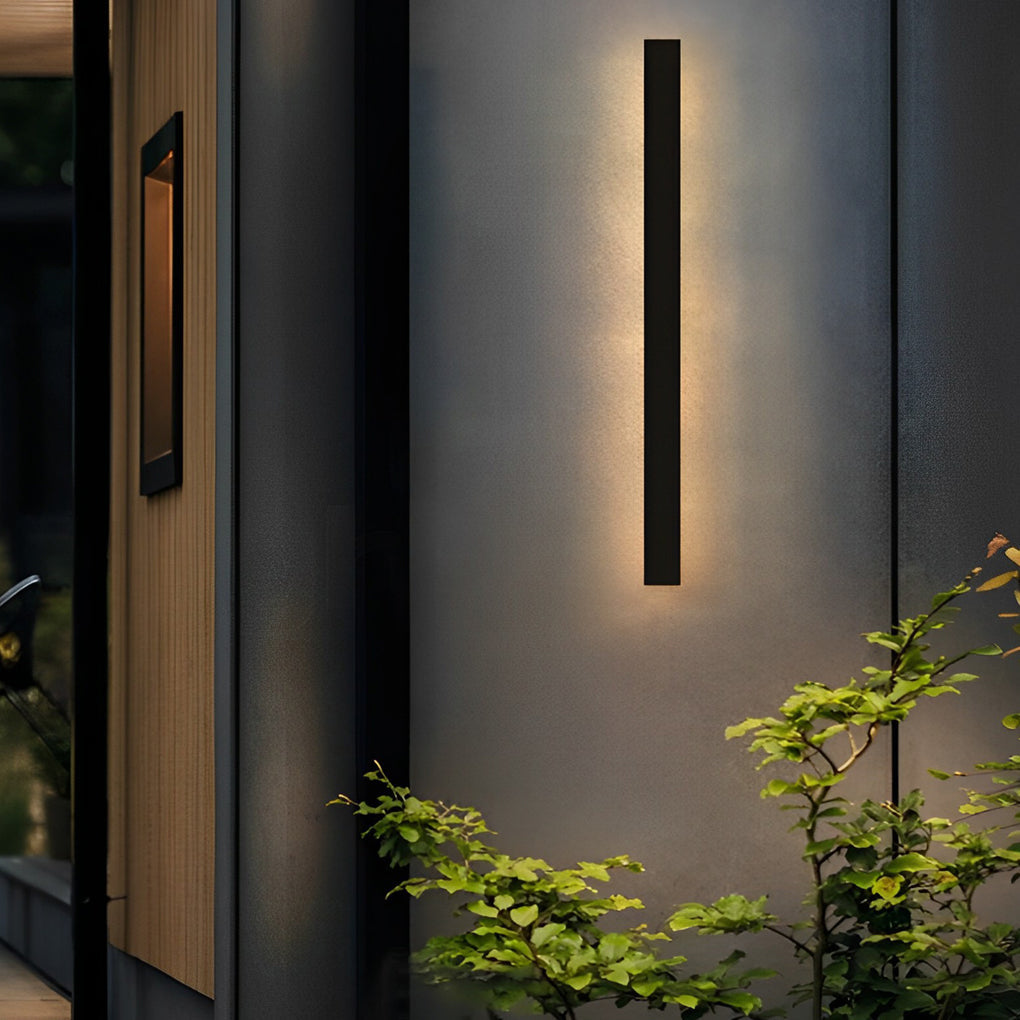 Outdoor linear wall light creating warm vertical glow on textured wall near garden plants.