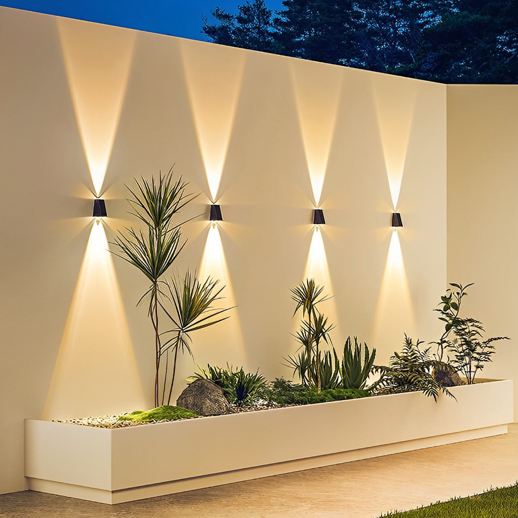Outdoor wall sconce up and down lighting adding ambiance to a garden wall with plants.