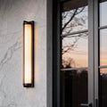 Outdoor wall sconces black mounted beside a modern entry door, featuring a slim rectangular frame with warm vertical light glow.